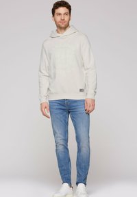 Hanorac gri deschis cu imprimeu grafic pe față, cu manșete ribbate și buzunar tip kangaroo, purtat cu blugi albaștri deschisi și adidași albi. Design simplu și casual.