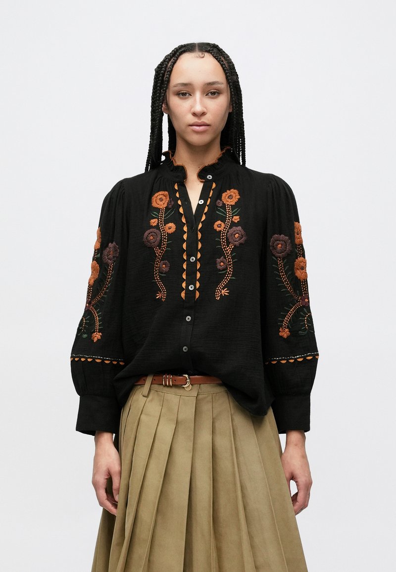 Črna srajčna bluza z zapenjanjem na gumbe, ki ima zapleteno cvetlično vezenje v oranžni in vijolični barvi, z nabrano izrezom in dolgimi napihnjenimi rokavi.