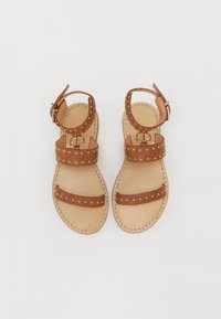 Brune skinnsandaler med to stropper med gullstikk, spenne lukking, og en lys fottøyle med sømdetaljer.