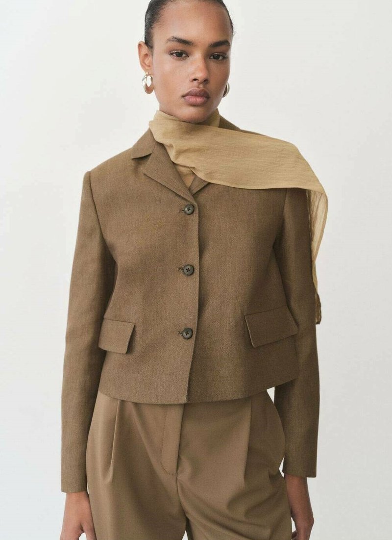 Brun kort blazer med en spetsad krage, två framfickor och tre knappar. Matchad med en ljusbrun scarf, på en modell mot en neutral bakgrund.