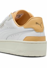 Baskets blanches avec une tige en cuir texturé et des accents orange, dotées d'un col rembourré et d'une semelle en caoutchouc avec une bande de roulement à motif.