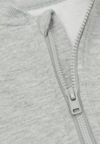 Giacca zip grigia chiara con una texture morbida, zip completa e un design del colletto ordinato. La zip e le cuciture sono di un grigio chiaro.