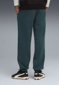 Teal sweatpants med elastiske manchetter, sidelommer og en afslappet pasform, båret med sorte og hvide sneakers med et markant logo.