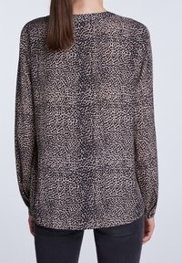 Langärmlige Bluse aus leichtem, beigem Material mit einem schwarzen Tierdruckmuster. Sie hat einen runden Ausschnitt und dezent geriffelte Ärmelabschlüsse.