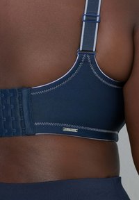 Donkerblauwe beha met verstelbare bandjes, haak- en oogsluiting en contrasterende stiksels. Voorzien van een logolabel op het bandje.