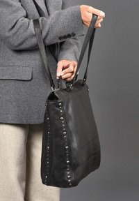 Zwarte leren tote bag met studaccenten, dubbele handvatten en een gestructureerde vorm. Voelt zacht aan met een gladde textuur.