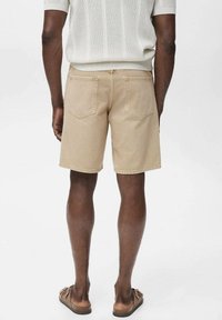 Beige denim shorts with a mid-length cut, featuring two back pockets and a slightly distressed texture. Worn with brown sandals.