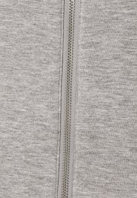 Felpa grigia con cerniera frontale, dalla texture liscia, dotata di una cerniera metallica argentata al centro. Il materiale sembra morbido e leggermente melangiato.