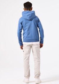 Blauwe hoodie met een grote capuchon, geribbelde manchetten en onderrand; gecombineerd met lichtgrijze cargobroeken en witte sneakers. Gladde stofstructuur.