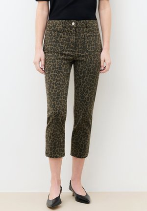 Vrouw die een cropped, nauwsluitende broek met luipaardprint draagt, voorzien van voorzakken en zwarte lage pumps met spitse neus.