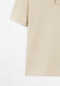 Beige polo skjorta med texturerad tyg, korta ärmar och klassisk krage. Den har ett subtilt mönster som betonar en neutral färgpalett.