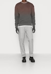 Sudadera gris degradado con cuello redondo, combinada con pantalones gris claro. Zapatos negros de cordones completan el conjunto. Fondo liso.