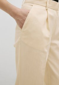 Beige op maat gemaakte broek met een gladde textuur, zijzak en subtiele verticale strepen. De tailleband is plat en sleek.