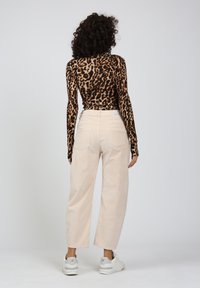 Langarmoberteil im Leopardenprint mit eng anliegendem Schnitt, kombiniert mit hellbeigen, weiten Hosen und weißen Sneakers. Glattes Material, lockerer Sitz.