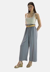 Pantalons larges gris clair avec une taille froncée, associés à un débardeur beige ajusté et des sandales compensées dorées. Des accessoires simples complètent le look.