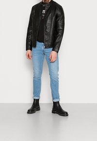 Svart läderjacka med kviltade axeldetaljer, bärs över en svart skjorta; matchas med ljusblå uppvikta jeans och svarta Chelsea-boots.