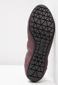 Chaussure bordeaux avec une semelle en caoutchouc texturé noir. La tige présente un tissu lisse avec des lignes courbées, mettant en avant un design minimaliste. Taille 37 marquée.