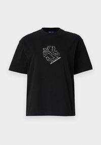 Lyhyet hihat musta T-paita, jossa on valkoinen geometrinen ompelusuunnittelu ja "Karl Lagerfeld Jeans" -teksti rinnassa.