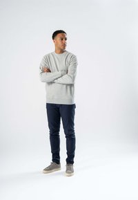 Grå sweatshirt med rund hals, parret med mørkeblå slim-fit bukser og grå sneakers. Stoffet ser blødt og struktureret ud.