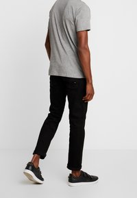 Grå kortærmet t-shirt parret med sorte denimjeans. Jeansene er rullet op ved anklerne, og sorte sneakers fuldender outfittet.