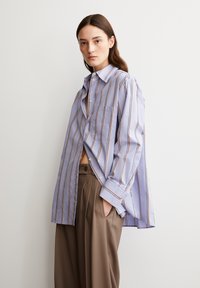 Gestreepte overhemd in lichtpaars met verticale strepen in oranje en crèmewit. Bevat een zak en heeft een ontspannen pasvorm, gedragen met een bruine broek.