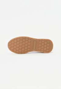 Semelle de chaussure avec une surface en caoutchouc texturé, présentant un motif en grille et un logo bien visible. Couleur brun clair avec un profil propre et plat.