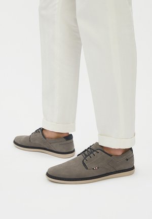 Šedé semišové šněrovací boty s námořnickým akcentem, kulatou špičkou a měkkou béžovou podrážkou, kombinované se světle béžovými kalhotami s ohrnutými nohavicemi.