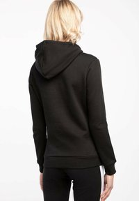 Hoodie nero realizzato in materiale morbido, con cappuccio regolabile e polsini a costine. Ha una vestibilità ampia e una texture liscia.
