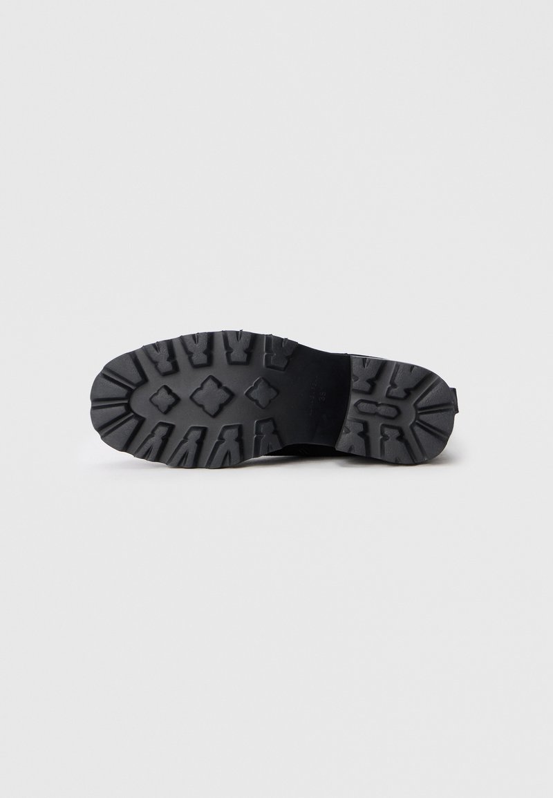 Suela de zapato de goma negra con un diseño texturizado que presenta surcos profundos y detalles en el patrón. Diseñada para ofrecer tracción y durabilidad.