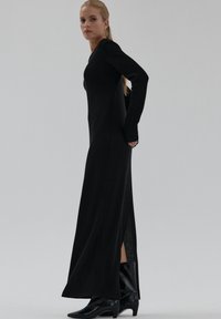 Czarna sukienka dzianinowa z długim rękawem, dopasowanym fasonem, bocznym rozcięciem i teksturowaną tkaniną. W połączeniu z czarnymi botkami na obcasie. Prosty, elegancki design.
