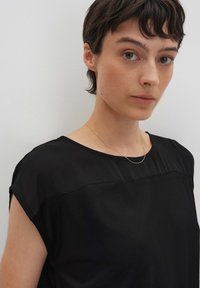 Top nero in tessuto liscio con maniche corte e un pannello trasparente nella parte anteriore. Presenta un collo rotondo e un design minimalista.