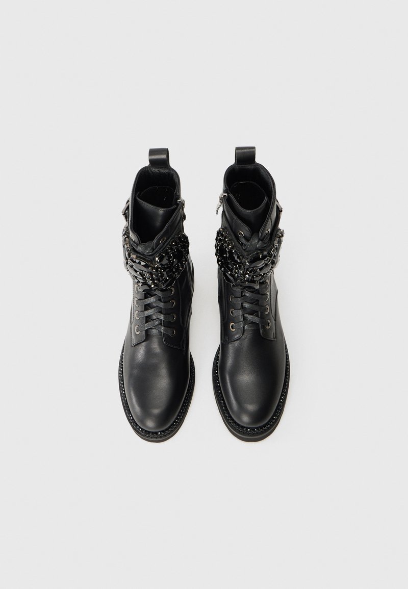 Stivali alla caviglia in pelle nera con punta arrotondata, lacci sulla parte anteriore e dettagli decorativi a catena vicino al polsino. Texture liscia e suola robusta.