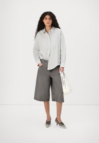 Camicia grigia chiara con righe sottili, abbinata a pantaloni corti grigi scuri fino al ginocchio. Scarpe argentate e una piccola borsa bianca.
