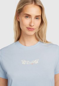 Light blue cotton t-shirt featuring a floral O'Neill logo in white. Round neckline and short sleeves with a smooth texture.