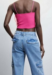 Top corto en rosa brillante con tirantes finos, combinado con pantalones cargo de mezclilla azul holgados que cuentan con grandes bolsillos laterales y traseros.