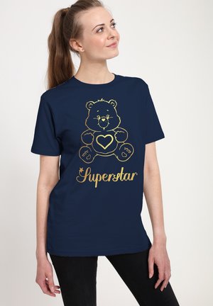 Marineblå t-shirt med et gyldent bjørnegraphic, der har et hjerte, og teksten "Superstar." Korte ærmer, standard pasform, glat bomuldsstruktur.