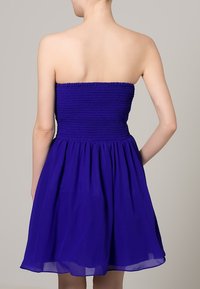 Fialové bezramínkové šaty s nařasenou korzetovou části a splývavou sukní vyrobené z lehké látky, zdůrazňující hladkou texturu.