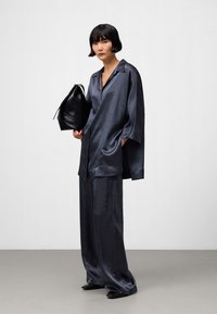 Marineblaues Satin-Pyjama-Set mit einer knopfbaren, locker sitzenden Bluse und weiten Hosen, kombiniert mit einer schwarzen Lederhandtasche. Glatte Textur, entspannter Stil.