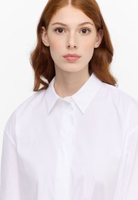 White button-up shirt with a classic collar, featuring a smooth texture and a clean front placket. The fabric appears lightweight and crisp.