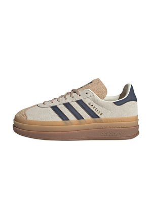 Low-top Adidas Gazelle sneaker in beige suede with navy stripes and cushioned layered gum sole.