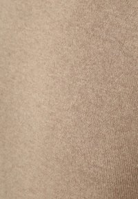 Beige gebreide stof, close-up, met een gladde textuur en een subtiele glans, en een consistent patroon over het hele oppervlak.
