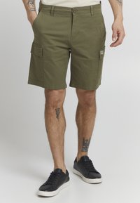 Shorts cargo vert olive à coupe droite, avec deux poches latérales et un tissu texturé. Portés avec des baskets noires.