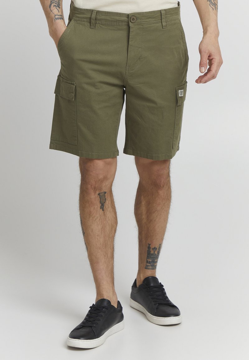 Shorts cargo vert olive à coupe droite, avec deux poches latérales et un tissu texturé. Portés avec des baskets noires.