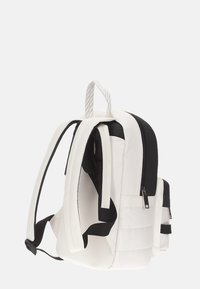 Zaino bianco e nero con spallacci imbottiti, maniglia di trasporto superiore e tasca frontale con zip, visto da un'angolazione laterale.