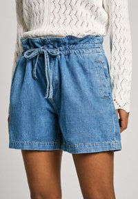 Pantalones cortos de mezclilla en azul claro con cintura elástica y cordón. Presenta bolsillos laterales y un corte relajado. Textura suave, diseño casual.