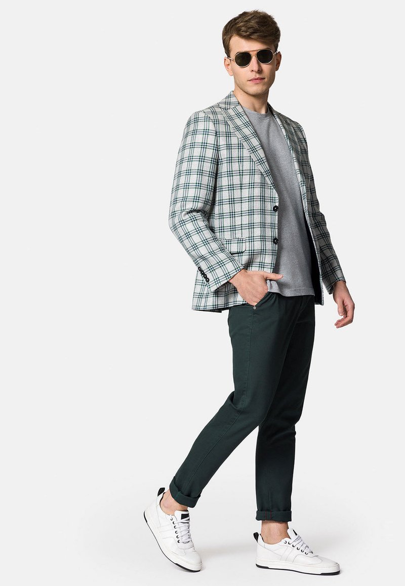 Marynarka w kratę w białym, zielonym i czarnym kolorze, szary t-shirt, ciemnozielone spodnie i białe trampki z czarnymi akcentami, stylizowane z okularami przeciwsłonecznymi.