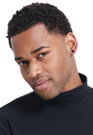 Black turtleneck top; short, curly hair; round black earring; smooth skin; neutral expression; focused gaze.
