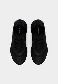 Ζευγάρι μαύρα αθλητικά παπούτσια Calvin Klein με κορδόνια και εσωτερικές σόλες με λογότυπο, εμφανιζόμενα από πάνω σε λευκό φόντο.