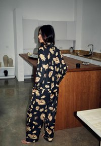 Pijamale negre cu modele grafice aurii, cu mâini, inimi și stele. Croială lejeră cu guler, dintr-un material neted și elegant.