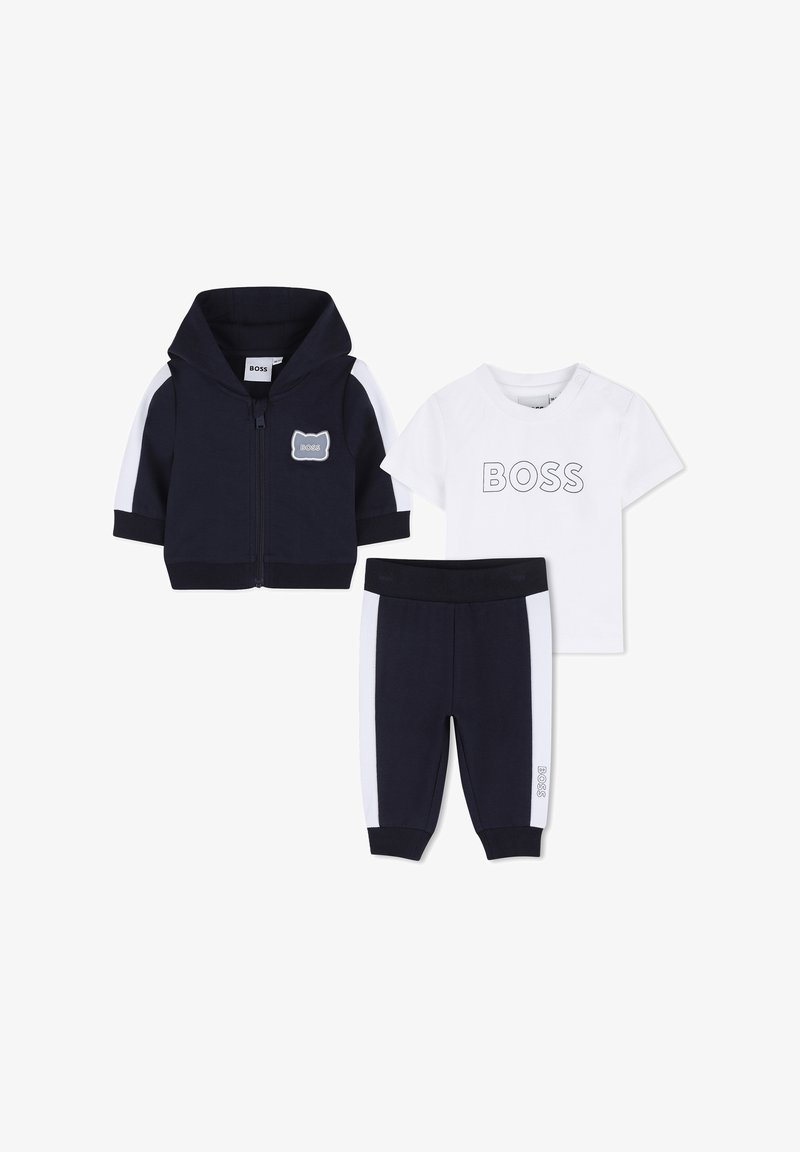 Marineblaue Kapuzenjacke mit Reißverschluss, weißes T-Shirt mit dem Schriftzug „BOSS“ und marineblaue Hose mit weißen Seitenstreifen und „BOSS“-Logo am Bein.